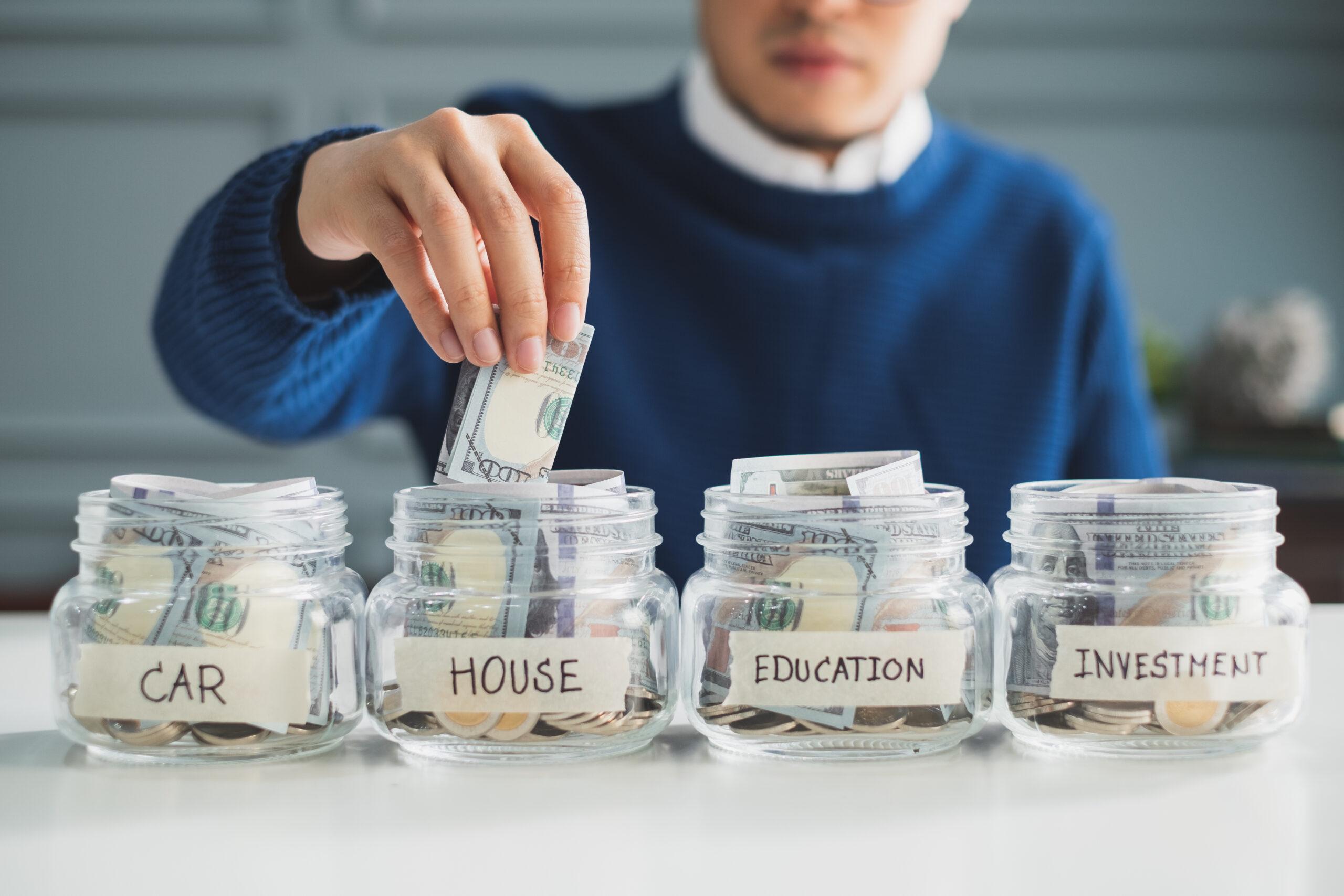 person choosing between jars labeled "car, house, education, and investment" with money in hand